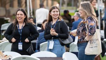 Three attendees smiling at each other, wearing their UC Tech swag bag.