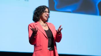 Keynote speaker, Raissa D'Souza, giving her keynote address at UC Tech. She is wearing a red suit.