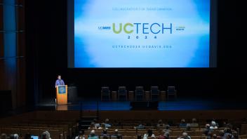 Andy Jones MC'ing at a podium with a UC Tech 2024 background.