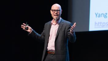 Keynote speaker, Martin Hilbert, giving his keynote address at UC Tech. Hilbert holds up one arm.
