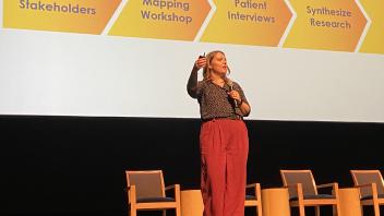 Kate McLoughlin giving her spotlight talk. She is standing with her presentation slides projected in the background.