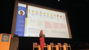 Kate McLoughlin giving her spotlight talk. She is standing with her presentation slides projected in the background.