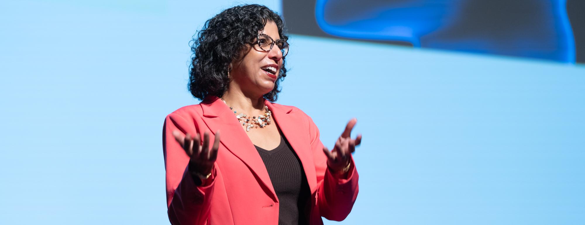Keynote speaker, Raissa D'Souza, giving her keynote address at UC Tech. She is wearing a red suit.