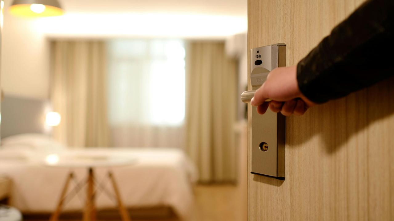 Arm opening a door to a hotel room with a bed in the background