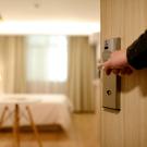 Arm opening a door to a hotel room with a bed in the background
